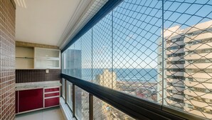 Un balcón con vistas al mar y a edificios, que presenta un revoque de azulejos, un armario rojo y una puerta de cristal.