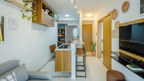 Una cocina moderna con una isla central, armarios de madera y microondas integrado. Hay una zona de estar con un sofá y una mesa de centro.