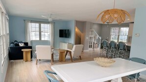 Een moderne woonkamer met een witte eettafel, blauwe stoelen, een bank en een plafondventilator.