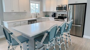 Een moderne keuken met witte kasten, een roestvrijstalen koelkast, een inbouwoven en een groot eiland met barstoelen.