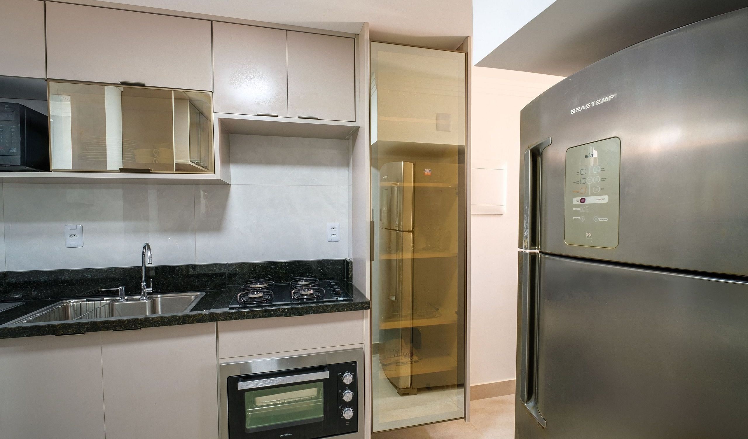 Eine moderne Küche mit Einbauofen, Edelstahlkühlschrank und einem Vorratsschrank mit Glastüren.