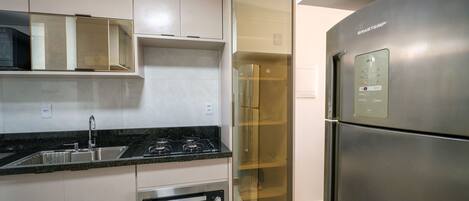 Eine moderne Küche mit Einbauofen, Edelstahlkühlschrank und einem Vorratsschrank mit Glastüren.