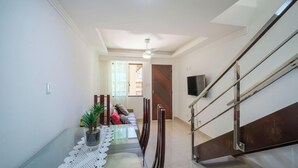 Un interno moderno con zona pranzo, tavolo in vetro, ventilatore a soffitto e scala con ringhiera in metallo.