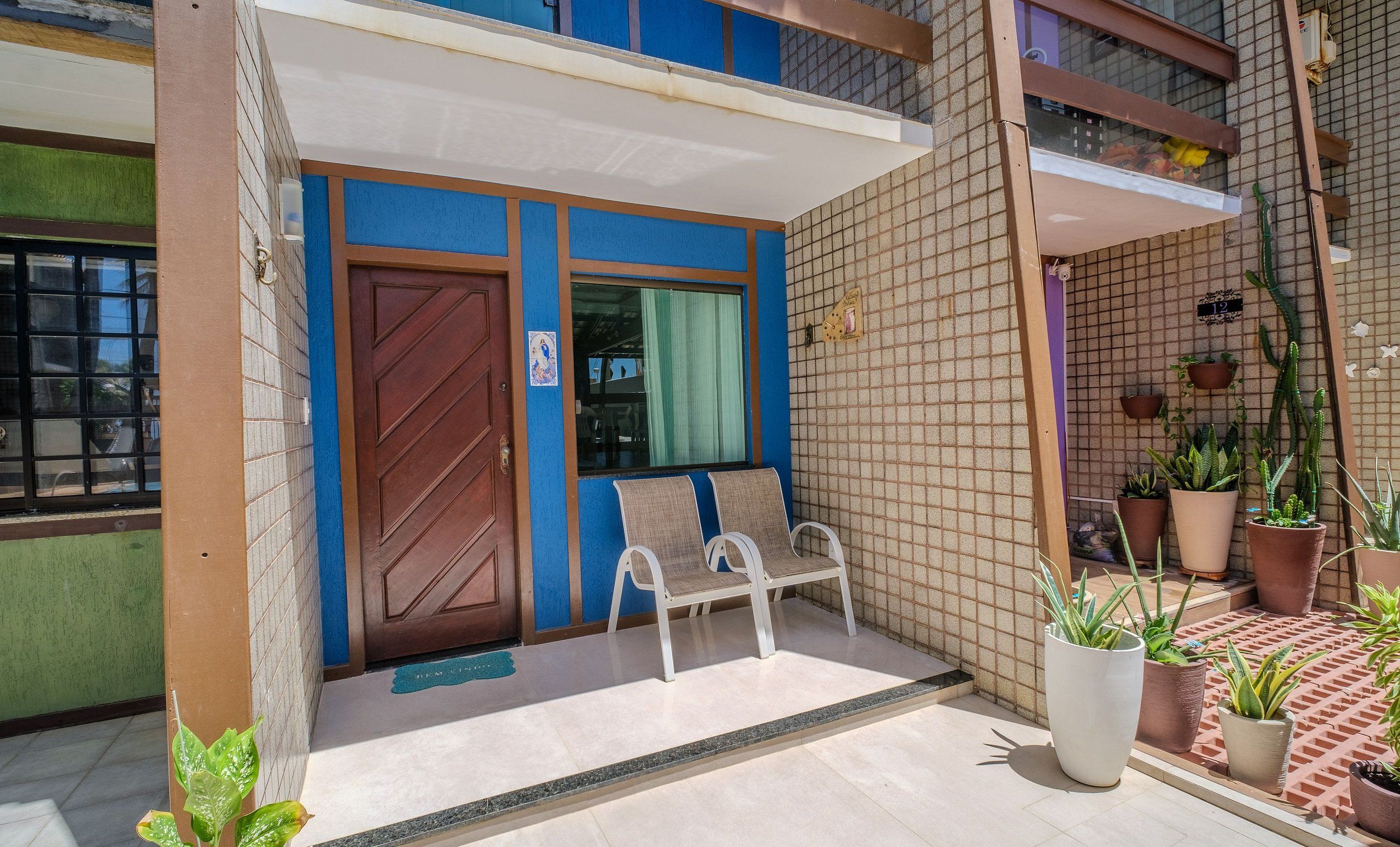 A building entrance with a blue door, two white chairs, and potted plants.
