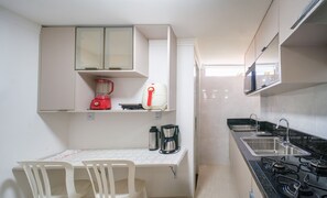 A compact kitchen with white cabinets, a red blender, a coffee maker, and a gas stove.