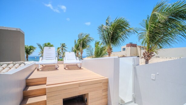 Una terrazza sul tetto con due poltrone bianche, un pontile di legno e palme.
