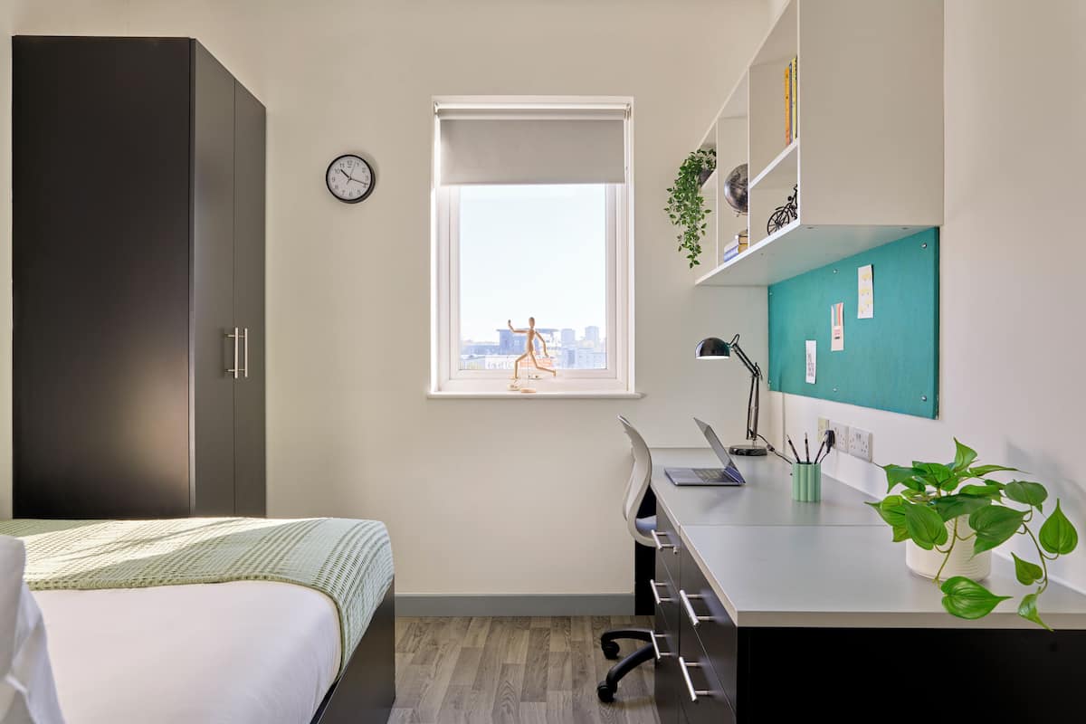 A modern bedroom with a bed, a desk, and a view of the city through a window.