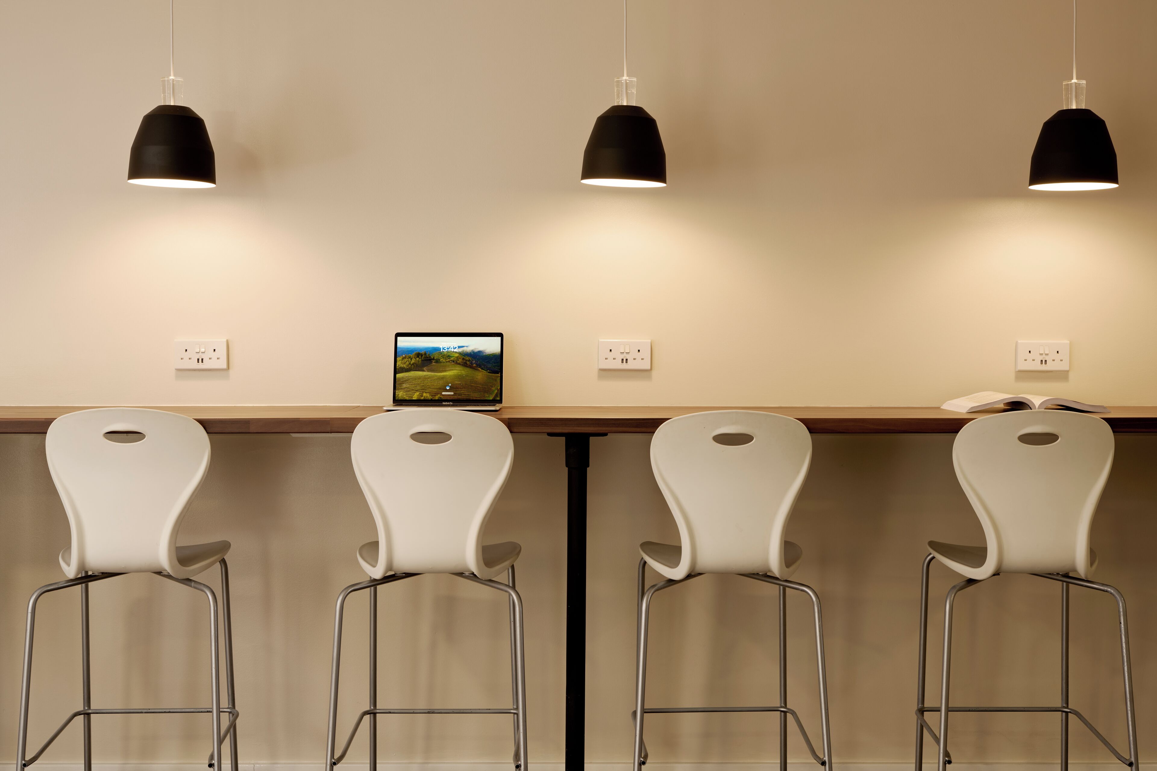 Un coin bar avec quatre tabourets de bar blancs, deux suspensions noires et un petit tableau encadré accroché au mur.
