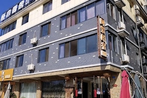 Un hotel de varios pisos con fachada moderna, unidades de aire acondicionado y una entrada visible.
