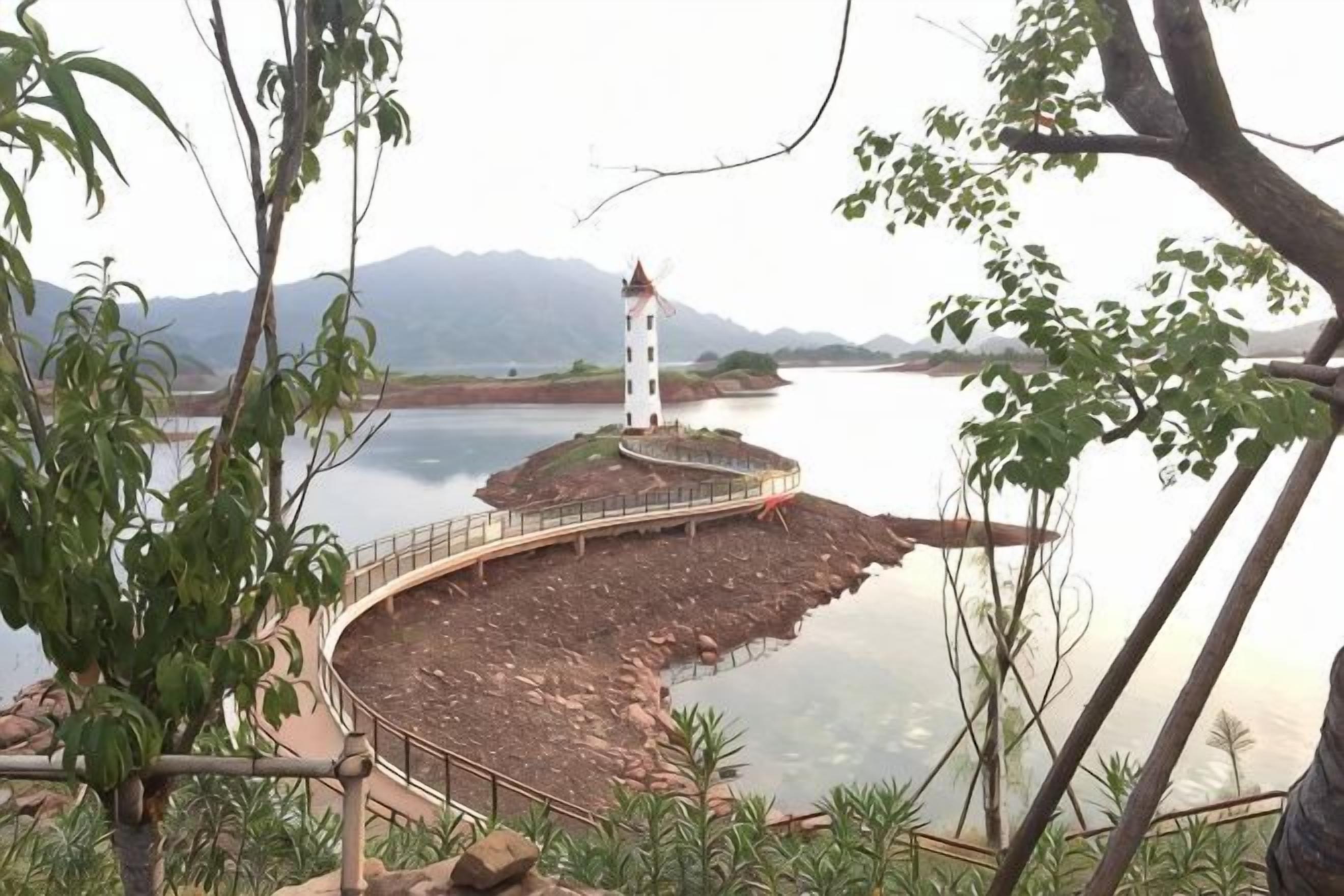 A lighthouse on a rocky island with a curved walkway leading to it, surrounded by water and greenery.