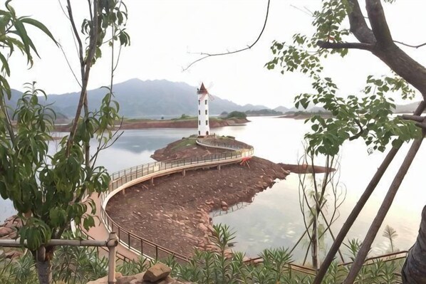 Un faro en una isla rocosa con un camino curvo que lo lleva, rodeado de agua y vegetación.