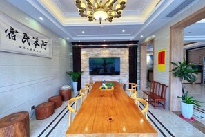 Un salón de conferencias con una larga mesa de madera, sillas, una pantalla de televisión y un candelabro.