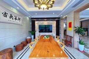 Un salón de conferencias con una larga mesa de madera, sillas, una pantalla de televisión y un candelabro.