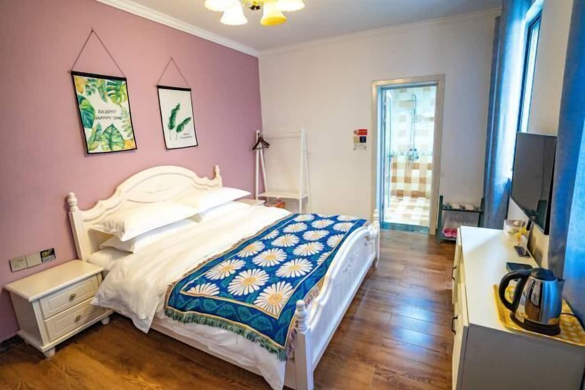 Un dormitorio con cama, mesita de noche y cómoda. Se ve una puerta que da a un baño.
