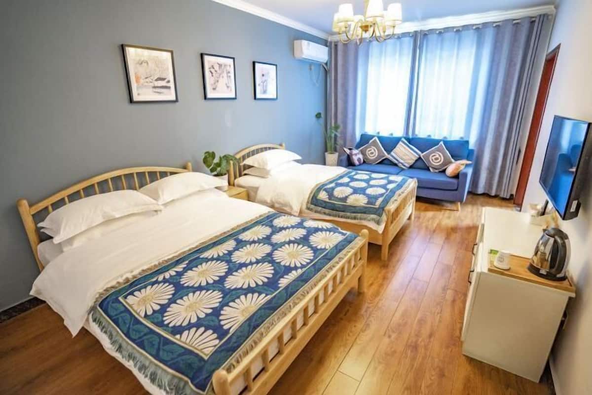 Una habitación con dos camas de madera, un sofá, televisión y una pequeña cocina.