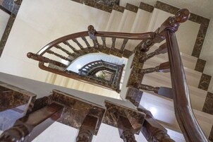 Una imponente escalera con barandilla curva y vista a un interior ornamentado.