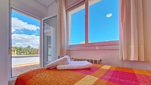 Quarto de hotel com cama, janela com cortinas e vista para a rua e prédios.