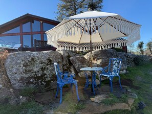 Un patio con una mesa, sillas y un gran paraguas, con un edificio de amplias ventanas al fondo.