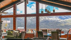 Une pièce chaleureuse avec de grandes fenêtres donnant sur les montagnes, des murs en bois et un coin repas équipé de chaises et de tables.