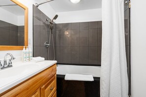 Un baño moderno con tocador de madera, un espejo grande, una bañera y una zona de ducha.