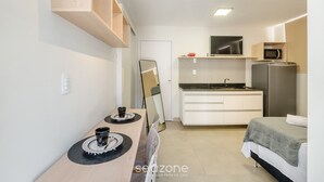 Habitación de hotel compacta con kitchenette, cama, mesa de comedor y espejo.