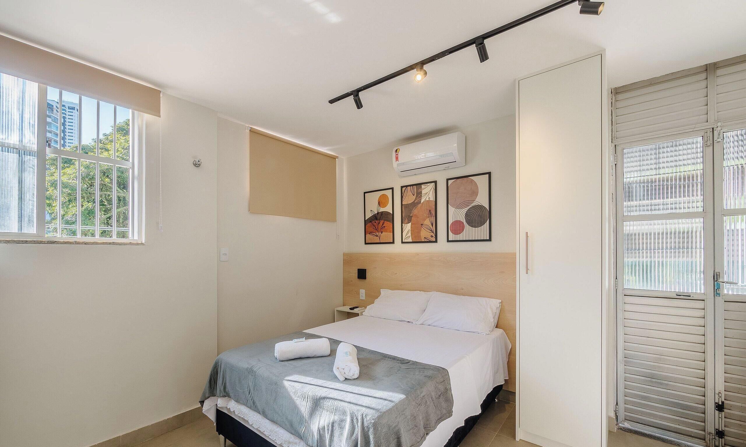 A hotel room with a bed, a window, an air conditioner, and a door.