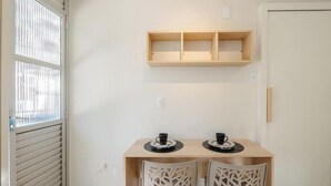 Un pequeño comedor con dos sillas blancas, una mesa de madera y un estante arriba.