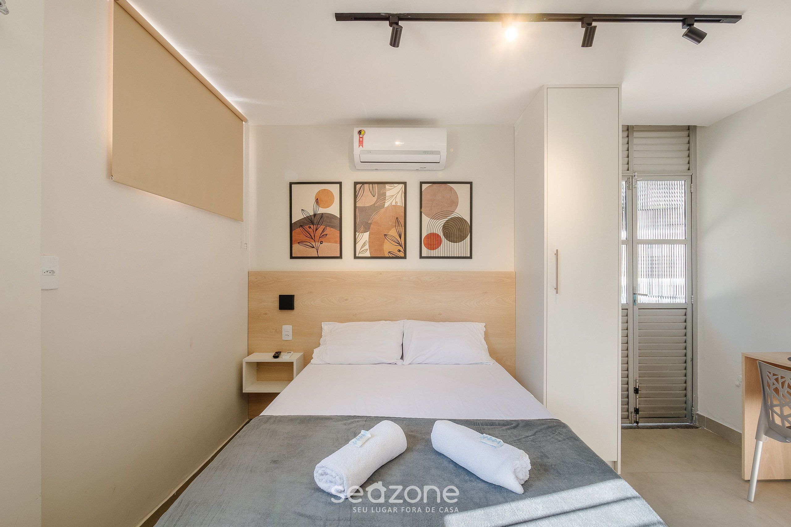 A hotel room with a bed, a desk, and a window with blinds.