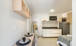A compact hotel room with a kitchenette, a bed, a dining table, and a mirror. - Studios 280m From Shopping Barra - ADE (Salvador)