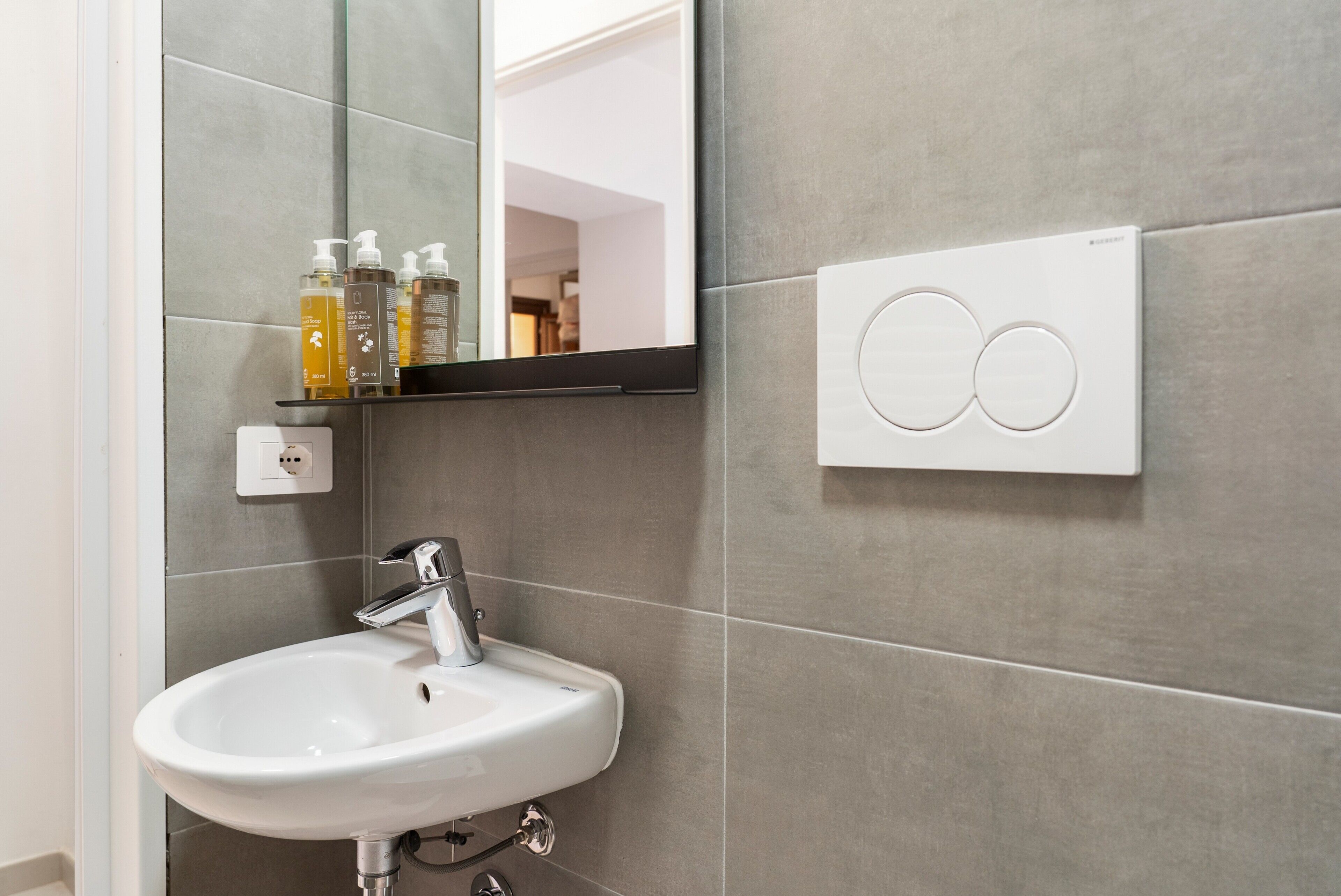 A bathroom with a white sink, a mirror, and a wall-mounted light switch.