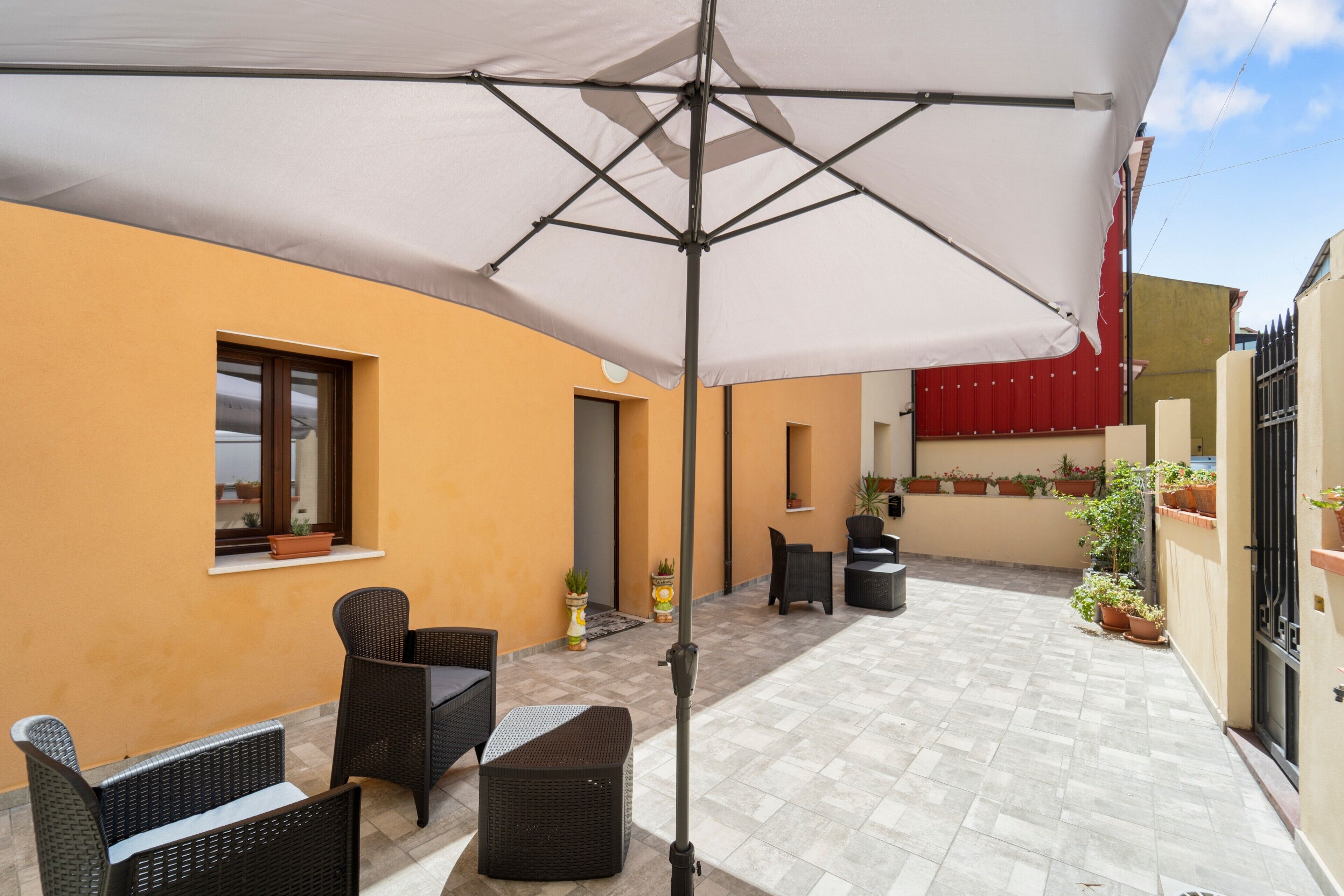 A patio area with outdoor furniture, a white umbrella, and potted plants.