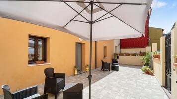 A patio area with outdoor furniture, a white umbrella, and potted plants.