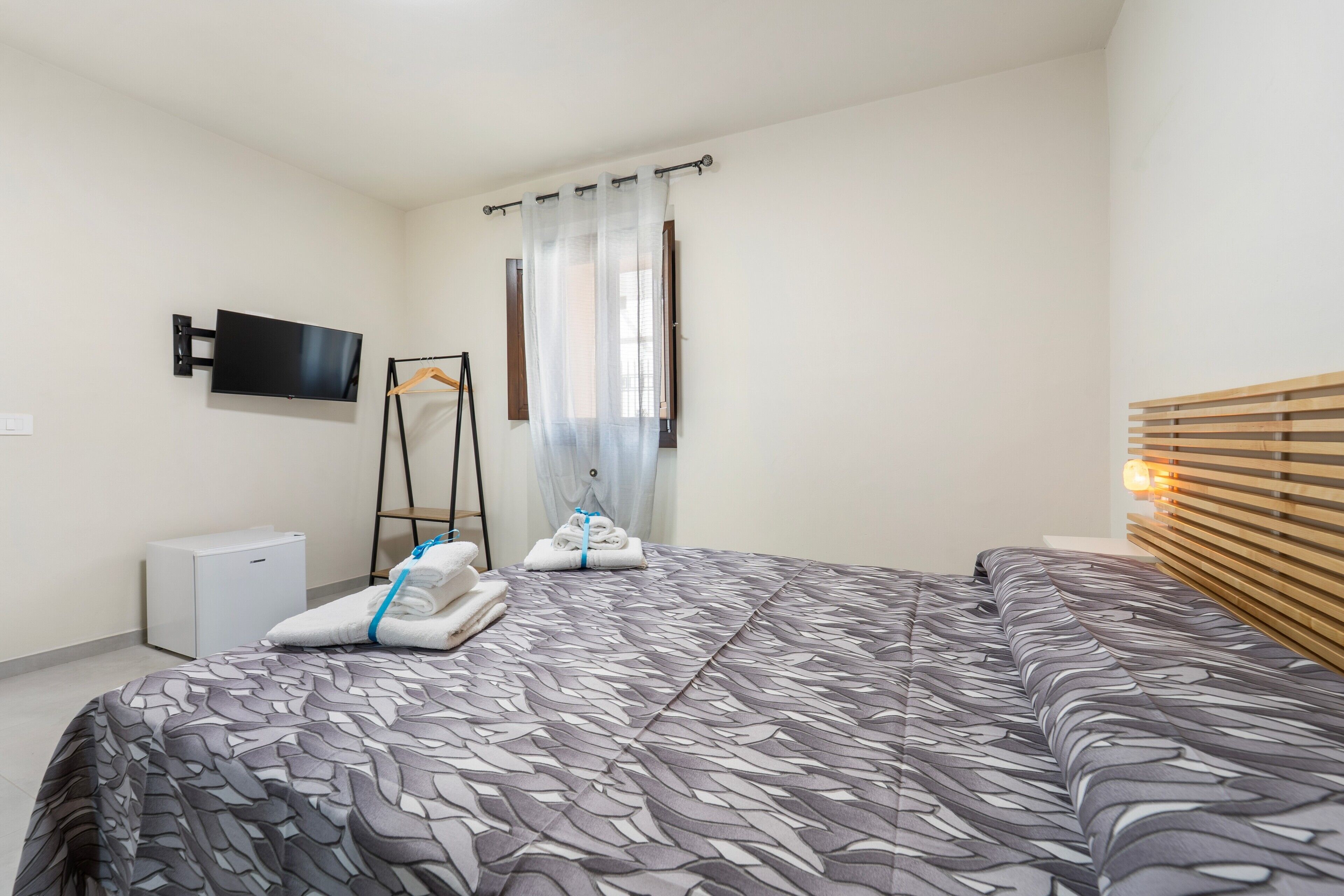 Ein Hotelzimmer mit Bett, Fernseher, einem kleinen weißen Schrank und einem Fenster mit Vorhängen.