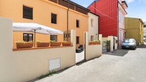 A residential building with a beige facade, a red section on the right, and a parked car. - Villa Giovia: Family Room 3 (Guspini)
