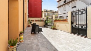 A courtyard with a tiled floor, outdoor furniture, potted plants, and a red building facade. - Villa Giovia: Family Room 3 (Guspini)