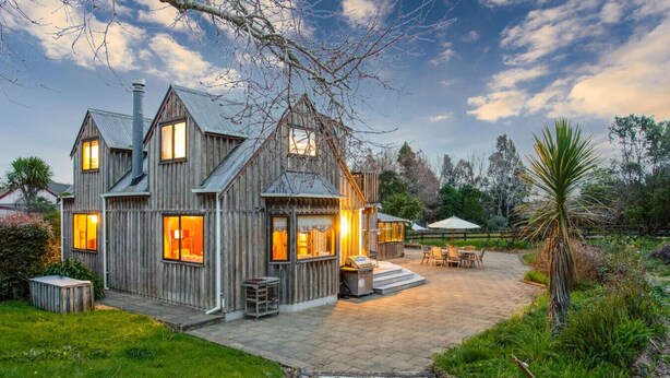 Een rustiek houten huis met veel ramen, een terras met tuinmeubilair en een verzorgde tuin.