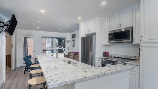 A modern kitchen with white cabinetry, a large island with stools, a stainless steel refrigerator, and a microwave. - Fall Line-Curate Telluride, Center of Town, Near Gondola, Parking Garage, HotTub (Telluride)
