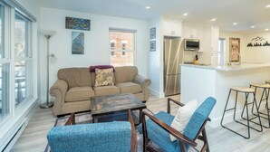 A modern living room with a sofa, a coffee table, and a blue chair. There is a kitchen area with a refrigerator, microwave, and bar stools. - Fall Line-Curate Telluride, Center of Town, Near Gondola, Parking Garage, HotTub (Telluride)