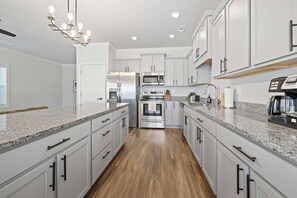 Una cocina moderna con armarios blancos, encimeras de granito, electrodomésticos de acero inoxidable y suelo de madera.