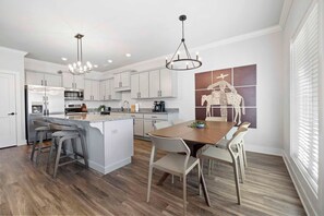 Una cocina moderna con armarios blancos, una isla central y un comedor con mesa y sillas de madera.