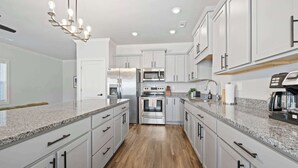 A modern kitchen with white cabinets, granite countertops, stainless steel appliances, and a wood floor.