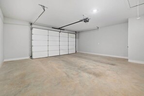 Un garaje con puerta blanca, proyector en el techo y suelo de hormigón.