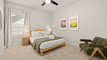 A bedroom with a bed, bedside lamps, a green armchair, and two framed pictures on the wall.