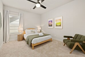 Un dormitorio con cama, lámparas de noche, un sillón verde y dos cuadros en la pared.