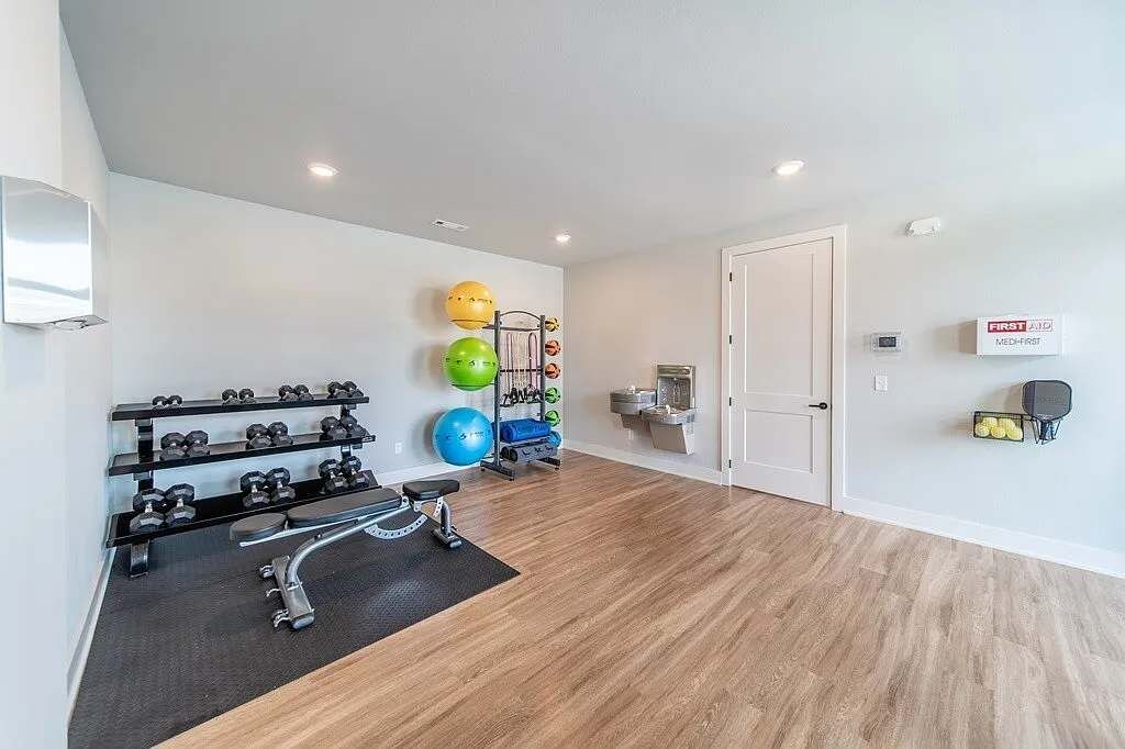 Ett modernt gym med träningsutrustning, ett väggmonterat ställ med hantlar och en dörr med en skylt.