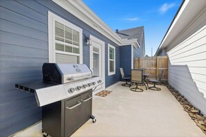 Un patio trasero con una parrilla integrada, cerca de madera y una mesa de patio con sillas.