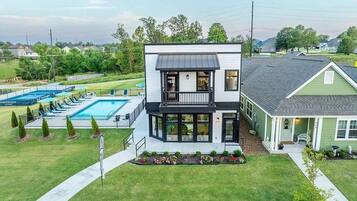 A two-story house with a balcony, a swimming pool, and a well-maintained lawn.