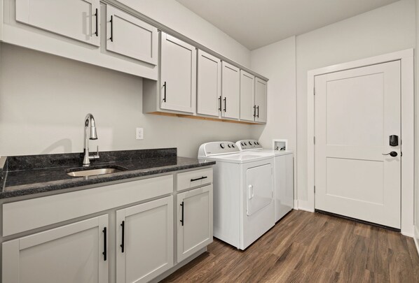 A kitchen with white cabinets, a granite countertop, a stainless steel sink, a built-in oven, and a white washing machine.