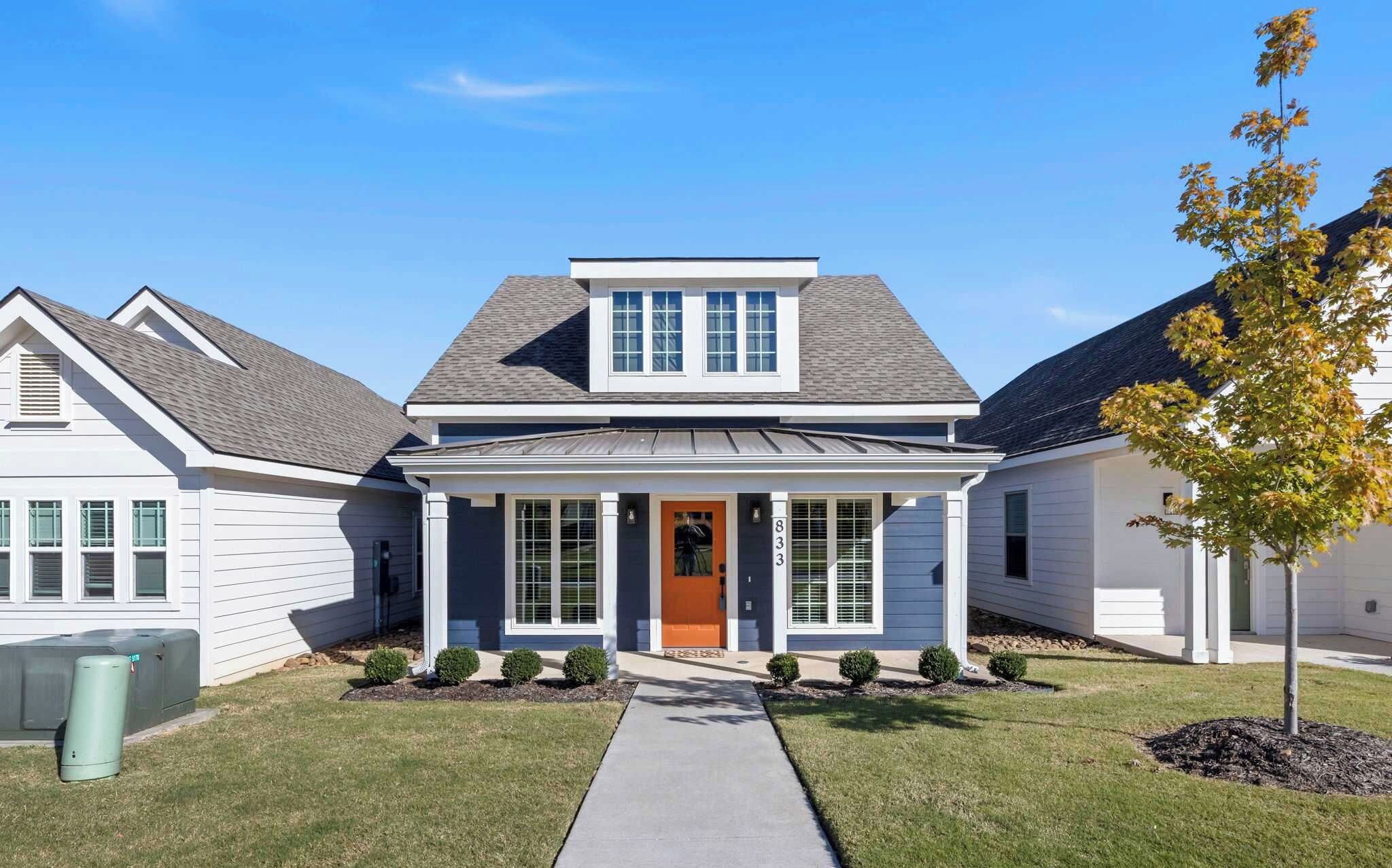 A two-story residential house with a front porch, a central door, and a small front yard with a tree.