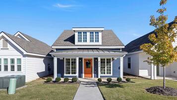 A two-story residential house with a front porch, a central door, and a small front yard with a tree.